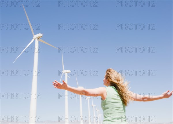 USA, California, Palm Springs, Coachella Valley, San Gorgonio Pass, Rear view of woman stretching arms and looking at wind turbines . Photo : Jamie Grill Photography