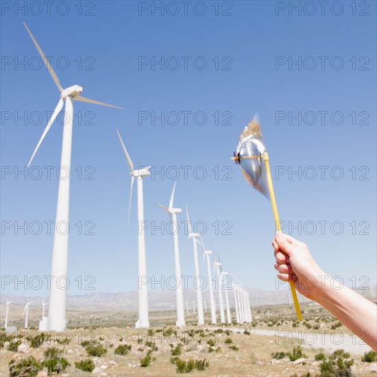 USA, California, Palm Springs, Coachella Valley, San Gorgonio Pass, Woman's hand holding pinwheel against blue sky and wind turbines. Photo : Jamie Grill Photography
