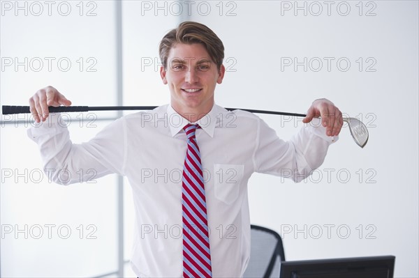 Portrait of young businessman holding golf club. Photo : Daniel Grill