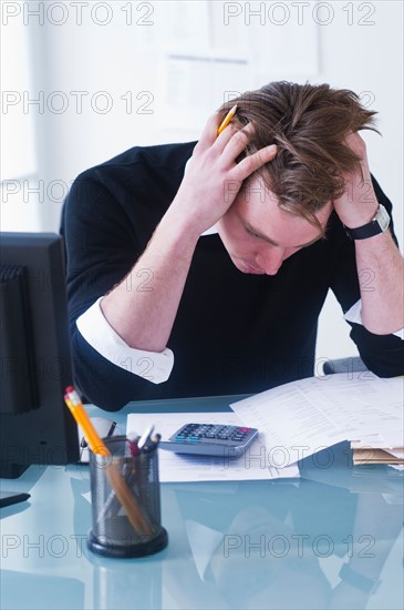 Man doing calculations holding head in hands. Photo : Daniel Grill