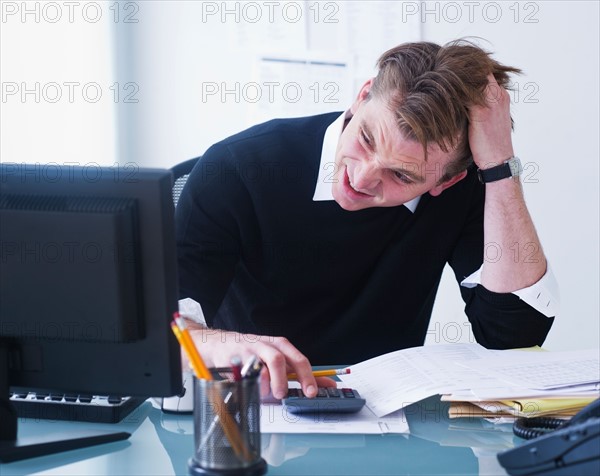 Man doing calculations holding head in hands. Photo : Daniel Grill