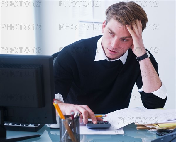 Man doing calculations holding head in hands. Photo : Daniel Grill