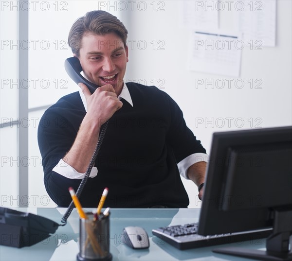 Man working on computer and talking on the phone at office. Photo : Daniel Grill