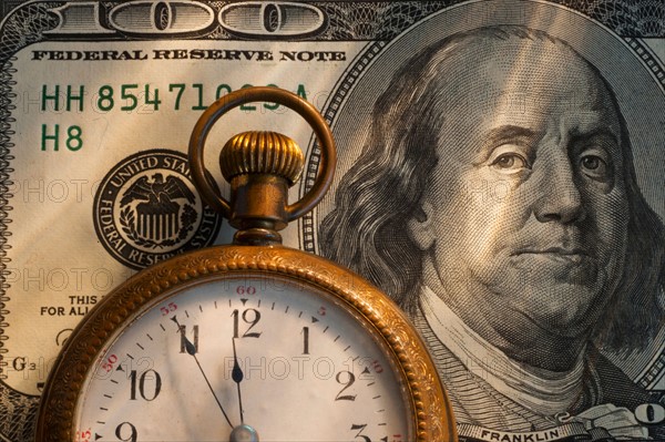 Pocket watch on one hundred dollar bill, studio shot.