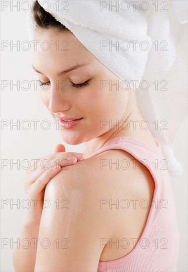 Young woman applying moisturizer on shoulder. Photo : Jamie Grill Photography