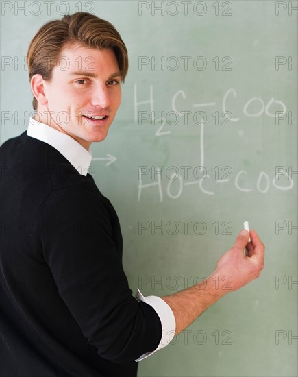 Young teacher writing equation on blackboard. Photo : Daniel Grill