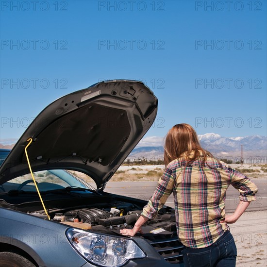 USA, California, Palm Springs, Woman standing in front of broken car in desert. Photo : Daniel Grill