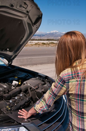 USA, California, Palm Springs, Woman standing in front of broken car in desert. Photo : Daniel Grill