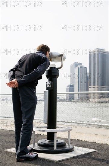 USA, New York City, Manhattan, man looking at skyline through telescope. Photo : Maisie Paterson