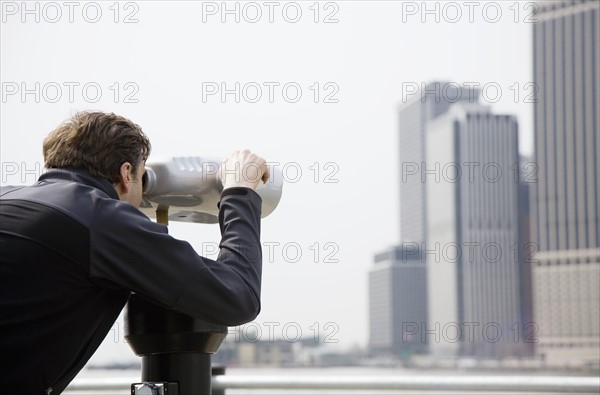 USA, New York City, Manhattan, man looking at skyline through telescope. Photo : Maisie Paterson