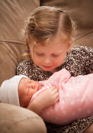 Portrait of girl (2-3) holding newborn girl (0-1months) . Photo : Mike Kemp