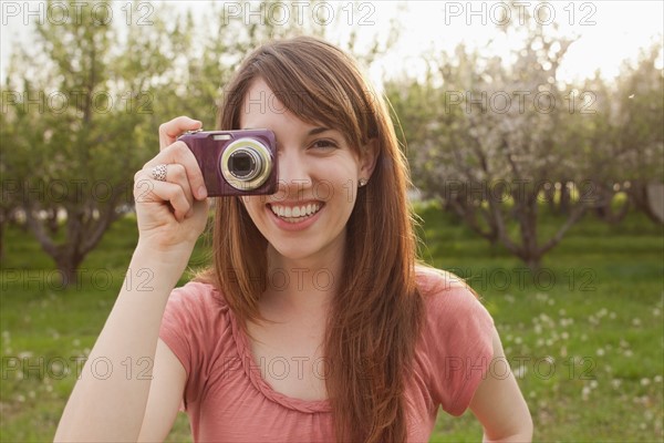 USA, Utah, Provo, Young woman holding digital camera in orchard. Photo : Mike Kemp