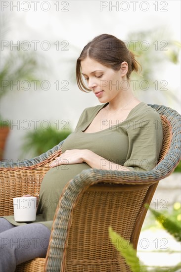 Pregnant woman sitting in wicker chair, touching belly. Photo : Rob Lewine