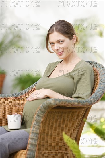 Pregnant woman sitting in wicker chair, touching belly. Photo : Rob Lewine