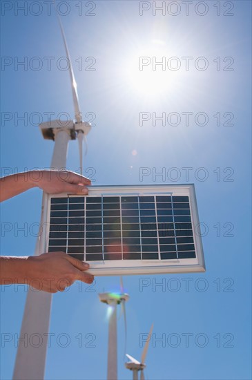 USA, California, Palm Springs, Woman's hands holding solar panel with wind turbines. Photo : Daniel Grill