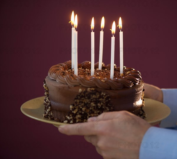 Studio shot of man holding chocolate birthday cake.