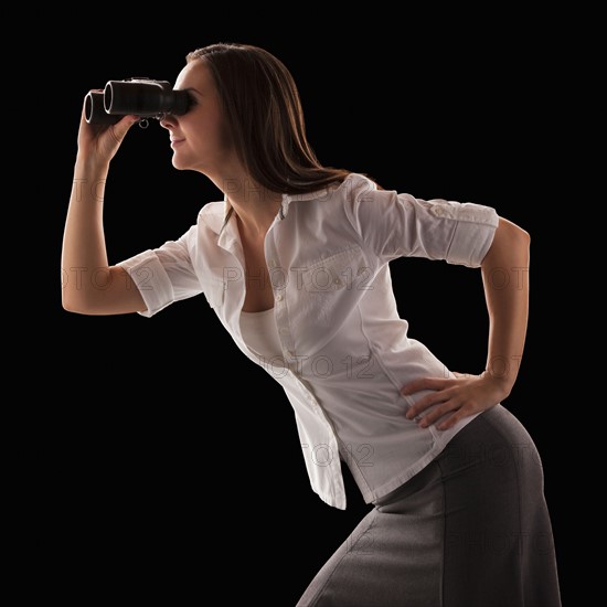 Young attractive businesswoman looking through binoculars. Photo : Mike Kemp