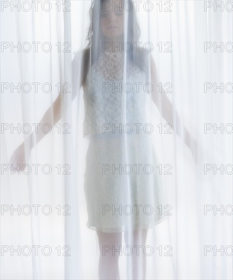 Portrait of young woman behind curtain.