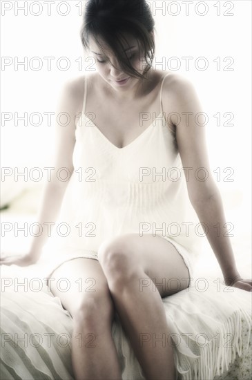Young woman in nightwear sitting on bed.