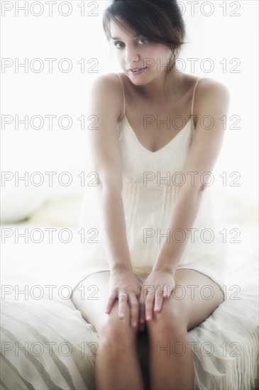 Young woman in nightwear sitting on bed.