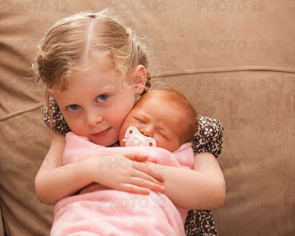 Portrait of girl (2-3) holding newborn girl (0-1months) . Photo : Mike Kemp