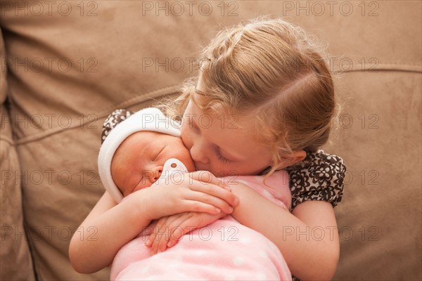 Girl (2-3) embracing baby sister on sofa. Photo : Mike Kemp