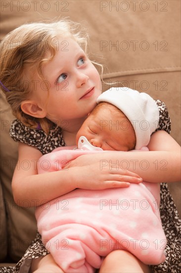 Girl (2-3) embracing baby sister on sofa. Photo : Mike Kemp