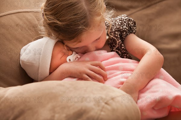 Girl (2-3) embracing baby sister on sofa. Photo : Mike Kemp