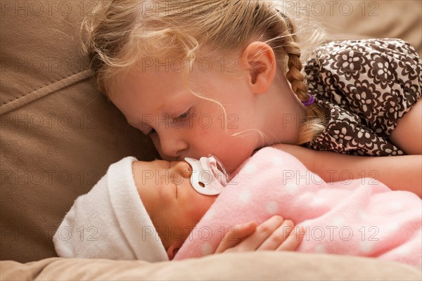 Girl (2-3) embracing baby sister on sofa. Photo : Mike Kemp