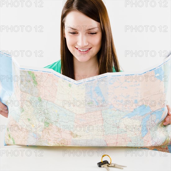 Young woman looking at map, car keys in foreground. Photo : Jamie Grill Photography