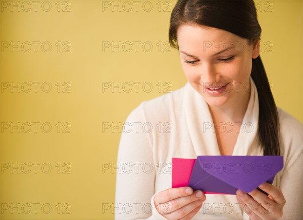 Smiling young woman holding letter. Photo : Jamie Grill Photography