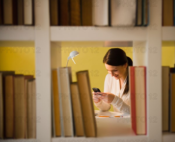 Young woman text messaging in library. Photo : Jamie Grill Photography