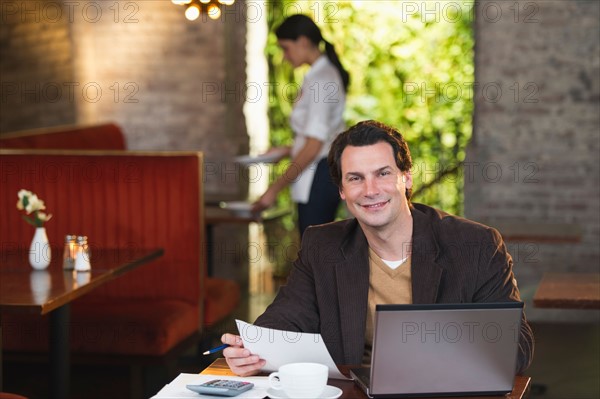 Owner working with laptop in restaurant with waitress in background.