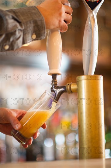 Barman poring beer from beer tap .