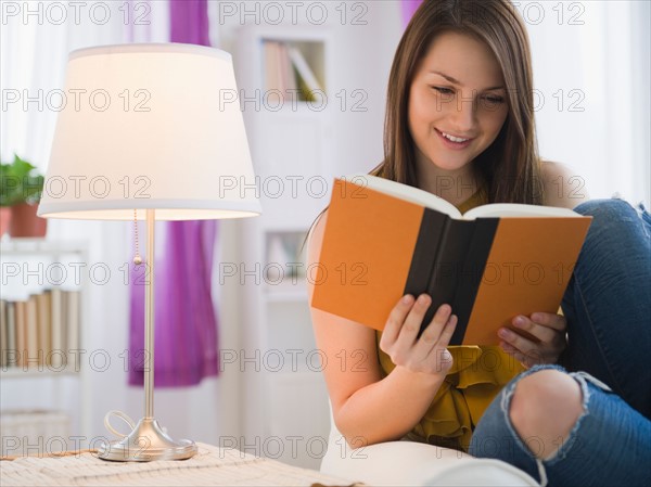 Young woman reading book in living room. Photo : Jamie Grill Photography