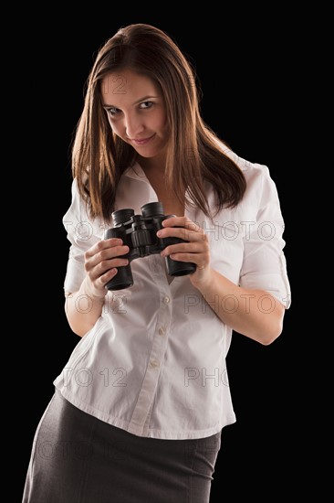 Young attractive businesswoman holding binoculars. Photo : Mike Kemp