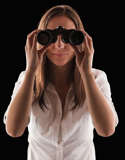Young attractive businesswoman looking through binoculars. Photo : Mike Kemp