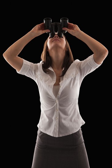 Young attractive businesswoman looking through binoculars. Photo : Mike Kemp