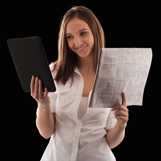 Young attractive businesswoman comparing financial results with financial column in newspaper. Photo : Mike Kemp