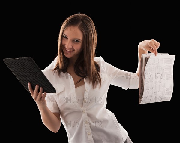 Young attractive businesswoman comparing financial results with financial column in newspaper. Photo : Mike Kemp