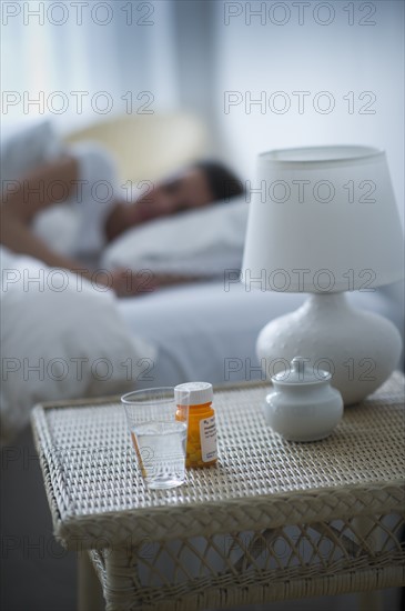 Sleeping pills bedside table with woman sleeping in background.