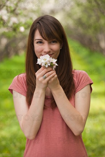 Young woman holding apple tree blossom in orchard. Photo : Mike Kemp