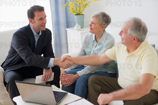 Senior couple talking to businessman in living room.