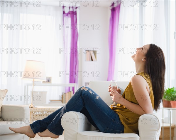 Young woman sitting on armchair with champagne flute. Photo : Jamie Grill Photography