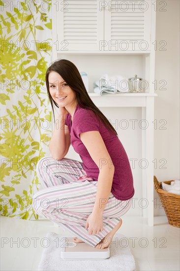 Young woman in pajamas crouching on scale. Photo : Jamie Grill Photography