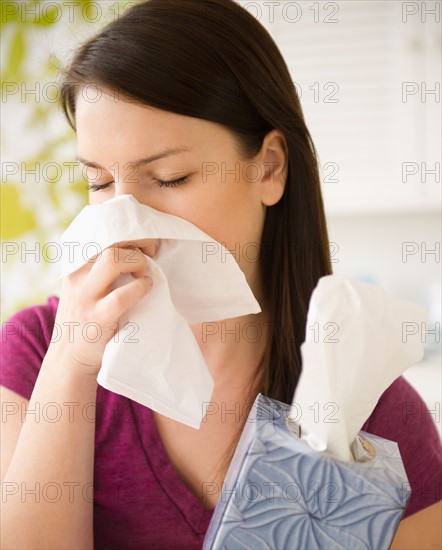 Young woman sneezing into tissue. Photo : Jamie Grill Photography