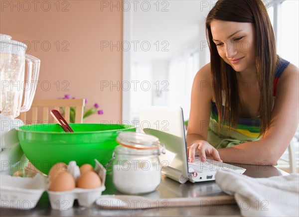 Young woman using laptop at kitchen table. Photo : Jamie Grill Photography