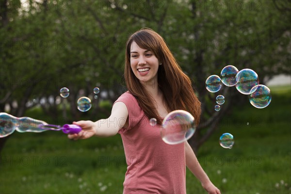 Young woman blowing bubbles in orchard. Photo : Mike Kemp