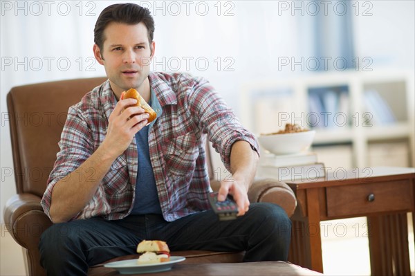 Man watching tv and eating sandwich.