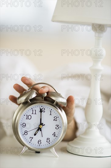 Close-up of man's hand reaching to alarm clock from bed.
